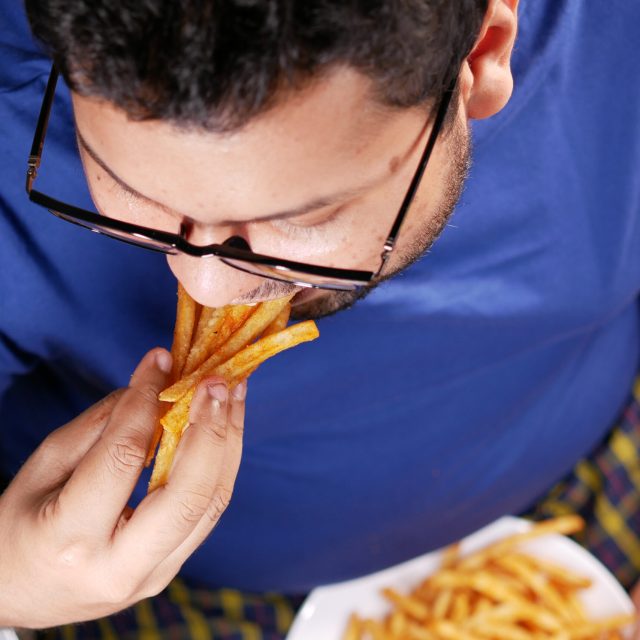 a fat man eating french fries while sited .