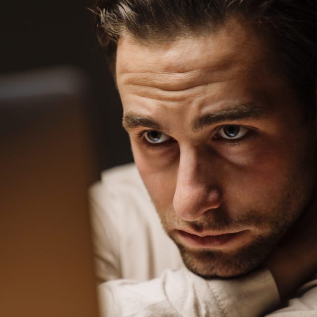 Tired bored mid aged brunette man looking at laptop screen while sitting in the office