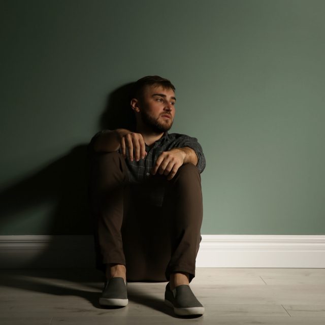 Depressed young man sitting on floor in darkness