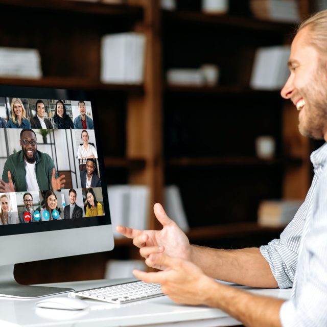 Successful caucasian young man talking on video conference with colleagues of different nationalities, discussing the project and strategy. Online business meeting, brainstorm of employees