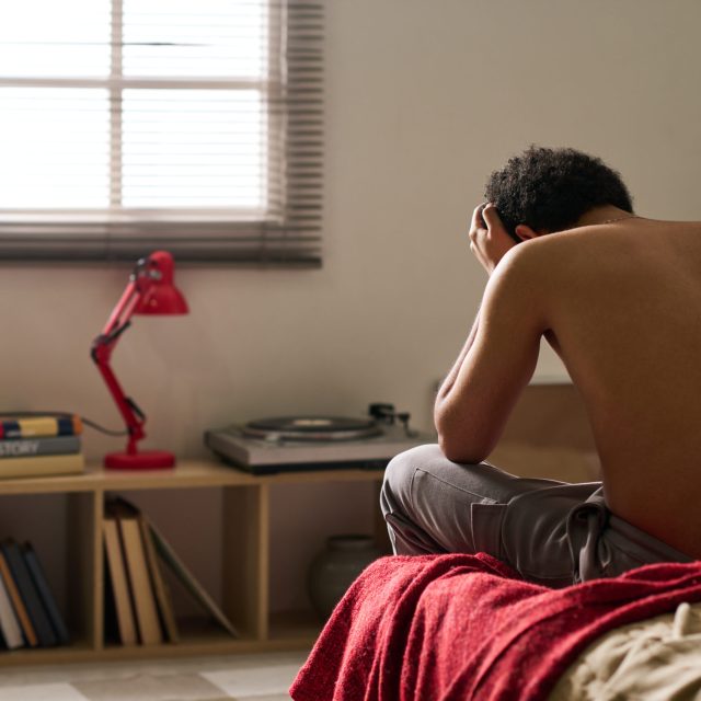 Rear view of young man in depression sitting alone in his bedroom and worried about his problems